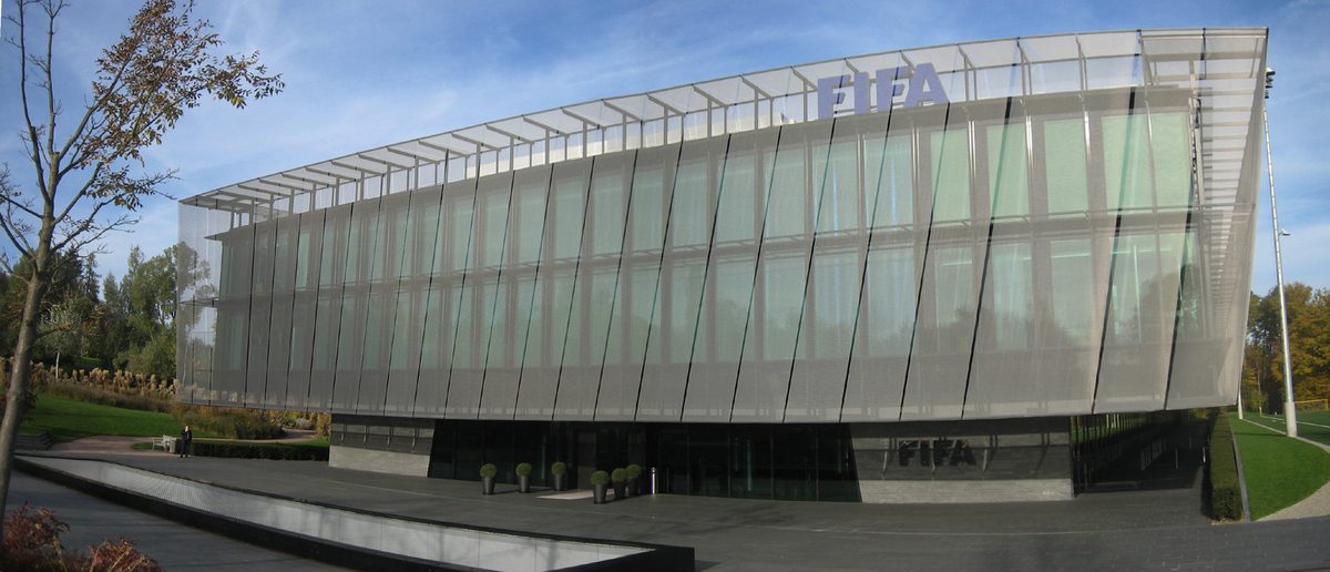 The Home of FIFA building in Zurich, a low glass-clad structure set in parkland with the FIFA wordmark on the facade