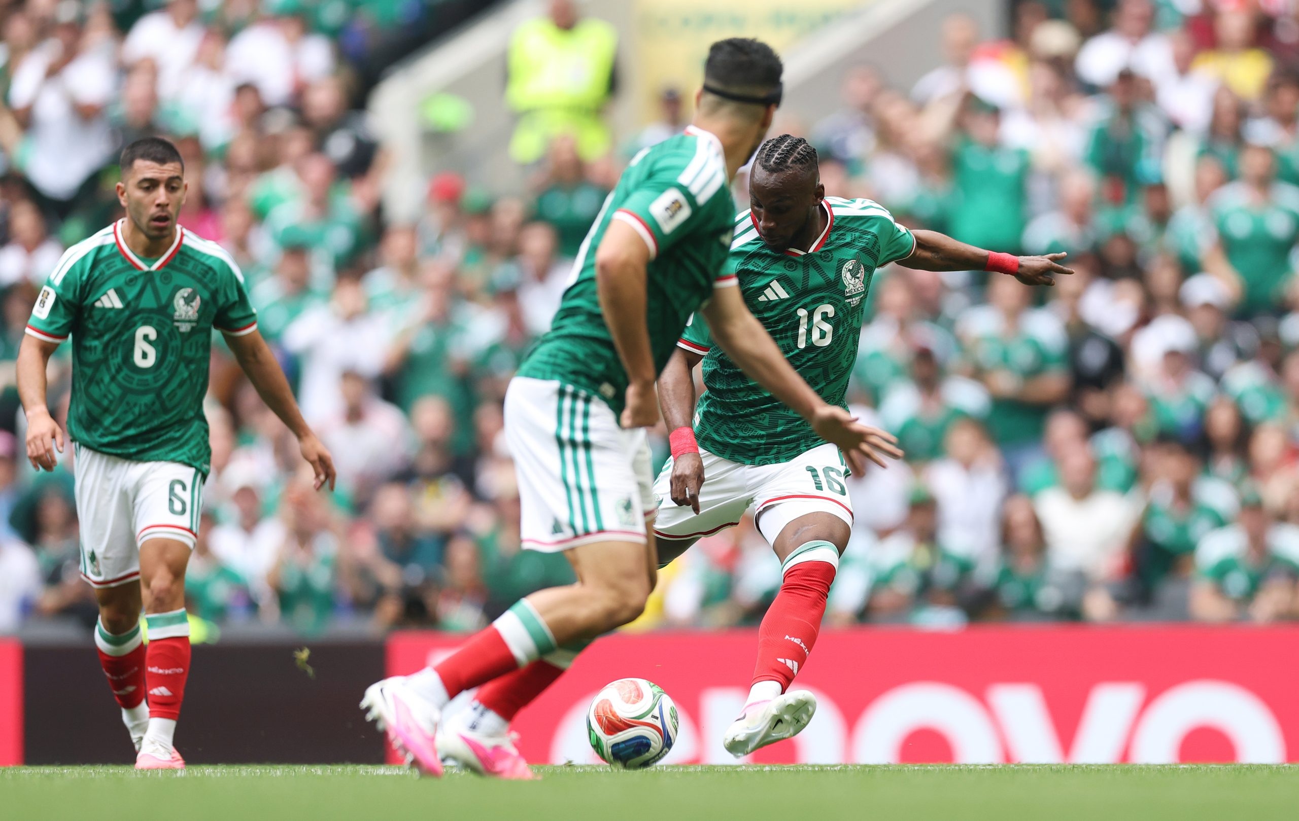 Mexico attack at the Estadio Azteca during the 2026 World Cup opening match against South Africa: a Mexico forward in the green home kit, number 16, shapes to shoot from just outside the penalty area while two team-mates and South African defenders close in, with a Lenovo perimeter advertising board behind the goal